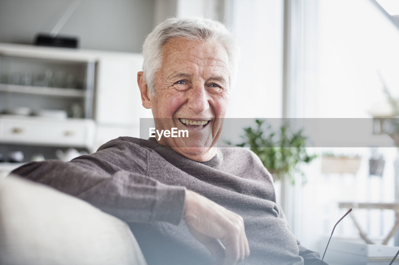 Portrait of happy senior man sitting on couch at home