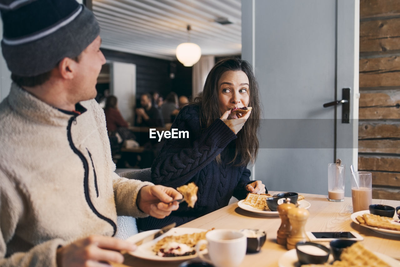 Woman eating breakfast while sitting with friend at table in log cabin