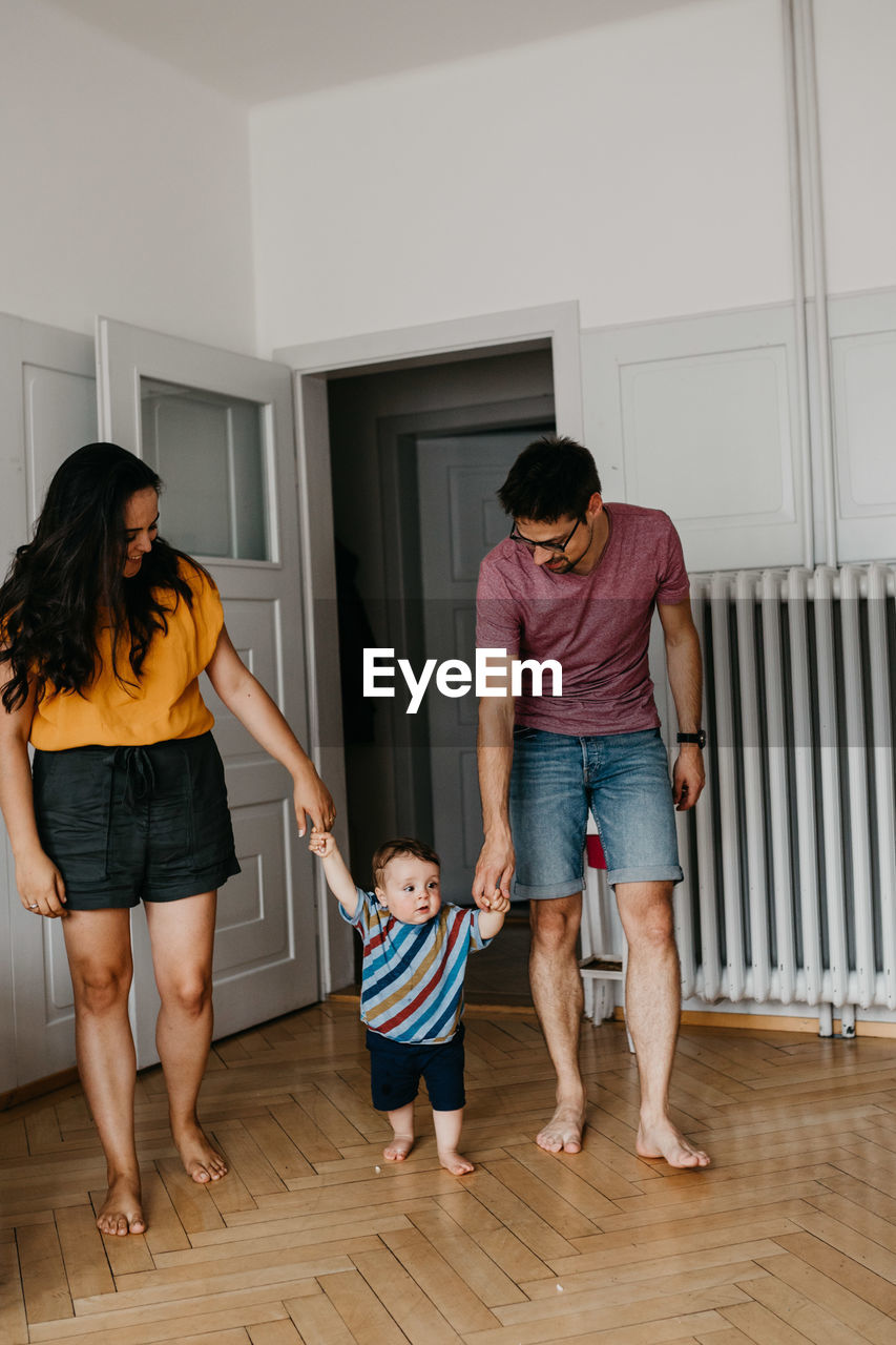 Parents holding hands with toddler son walking at home