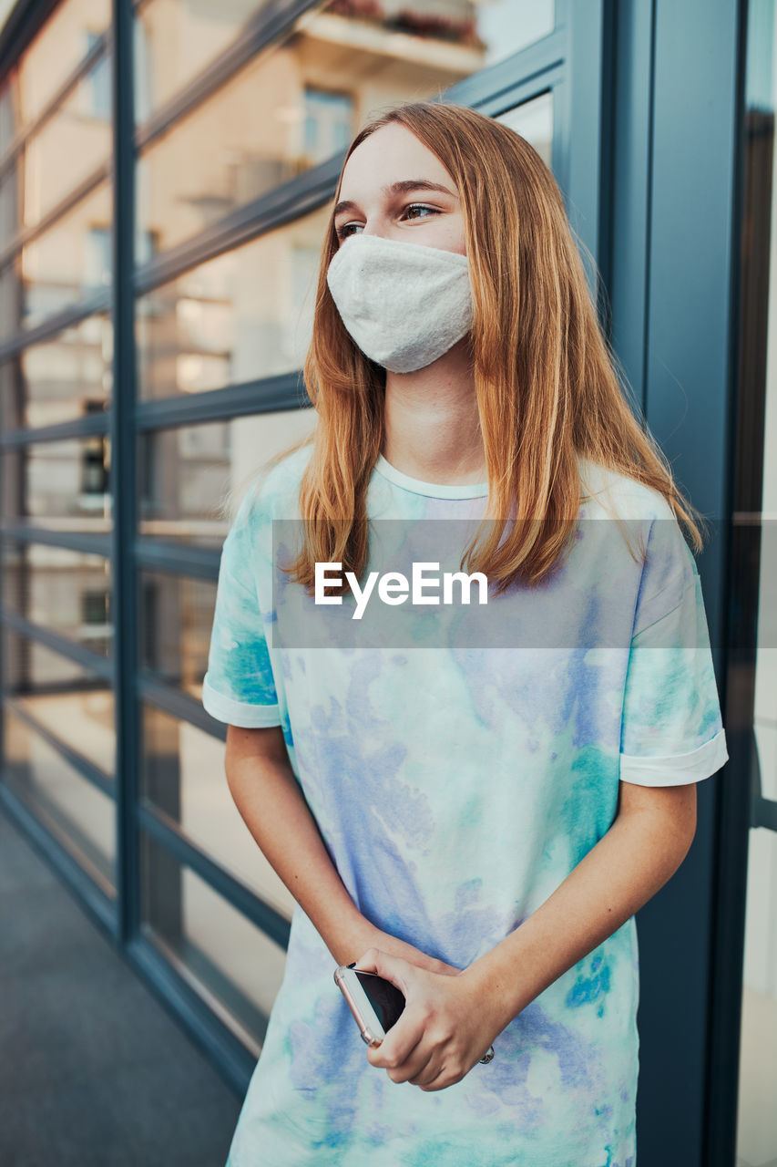 Girl wearing mask looking away while standing outdoors