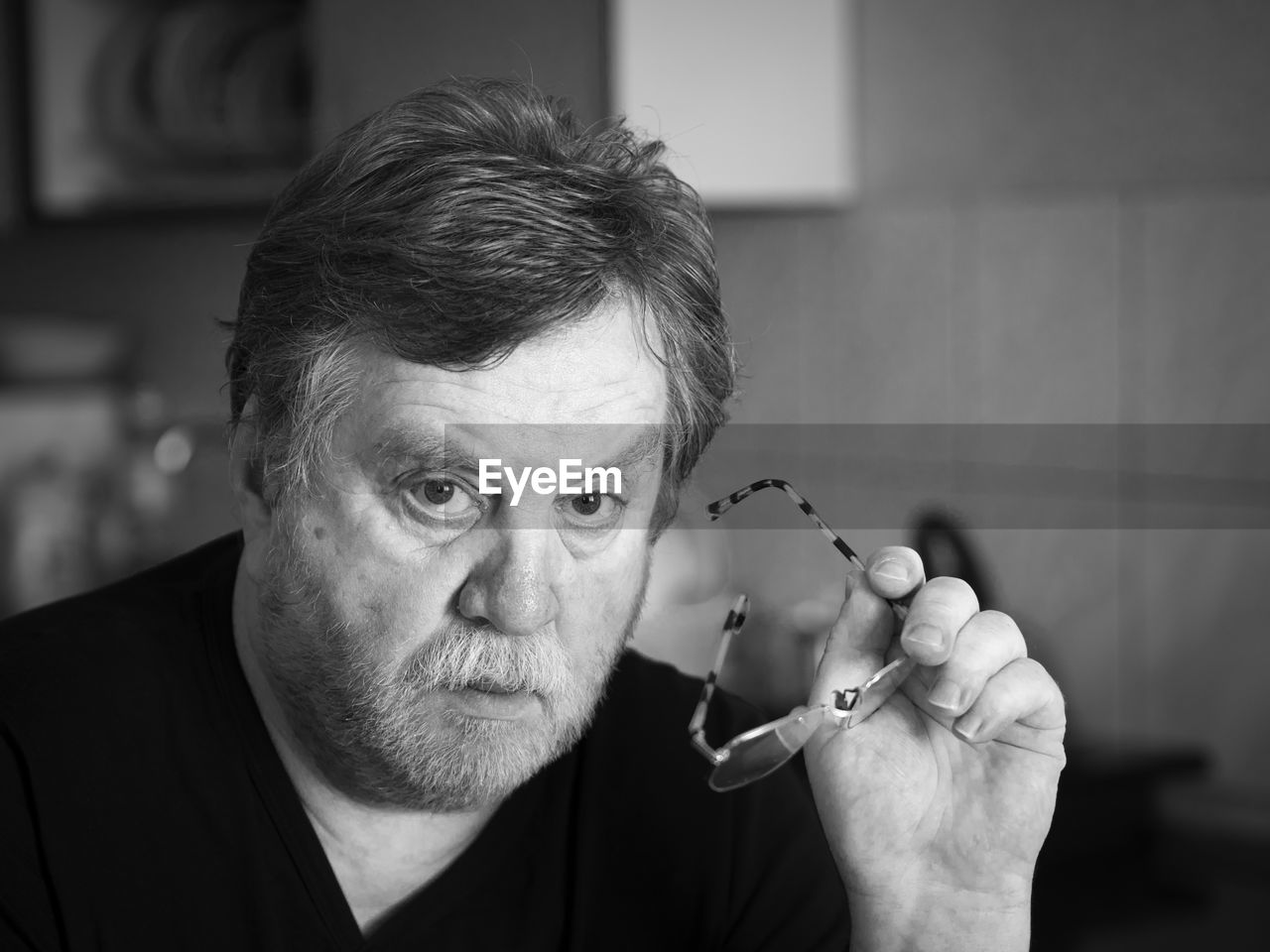 Close-up portrait of senior man holding eyeglasses at home