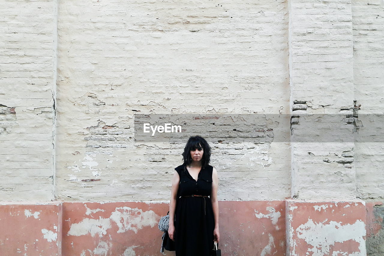 Portrait of young woman standing against wall