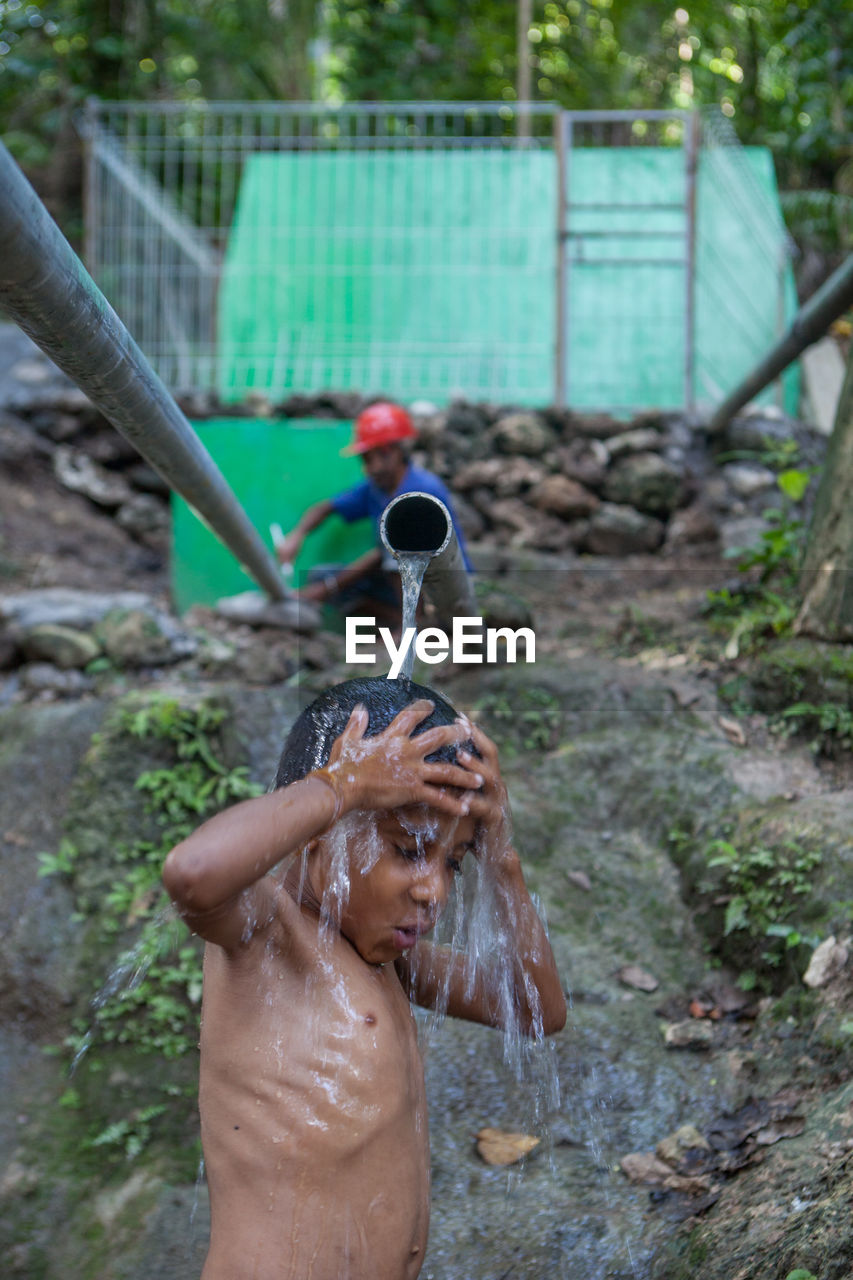 Shirtless boy standing under falling water from pipe