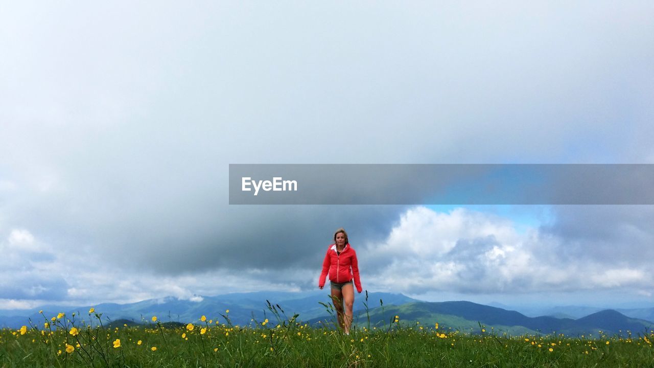 Young woman walking on grassy field against cloudy sky