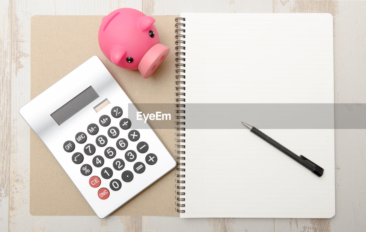 Directly above shot of calculator with piggy bank and pen on spiral notebook