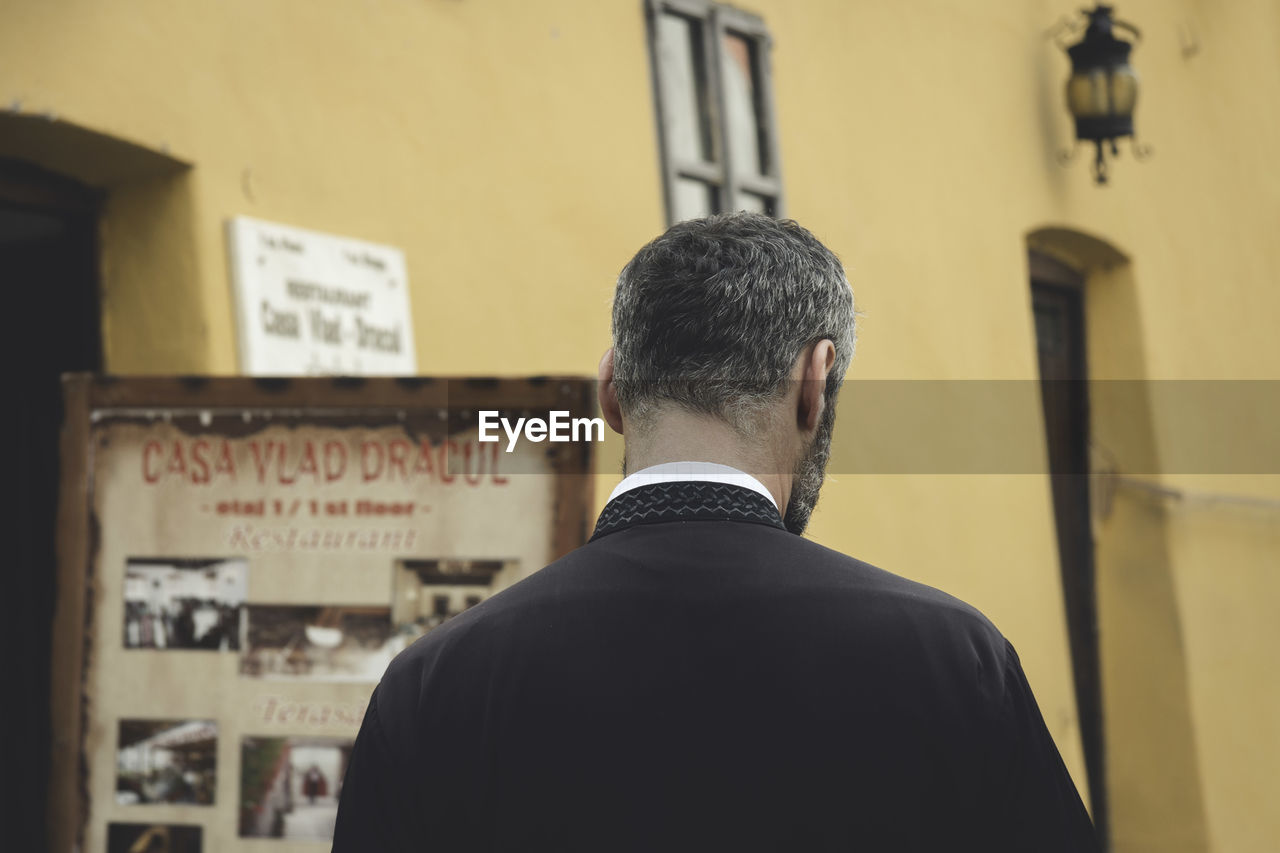 Rear view of man standing against yellow building