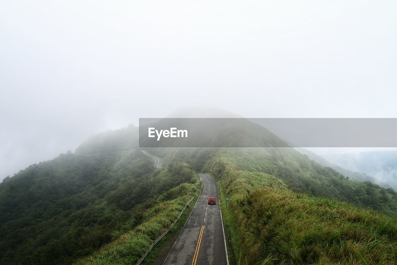 Car on road leading towards mountain against sky during foggy weather