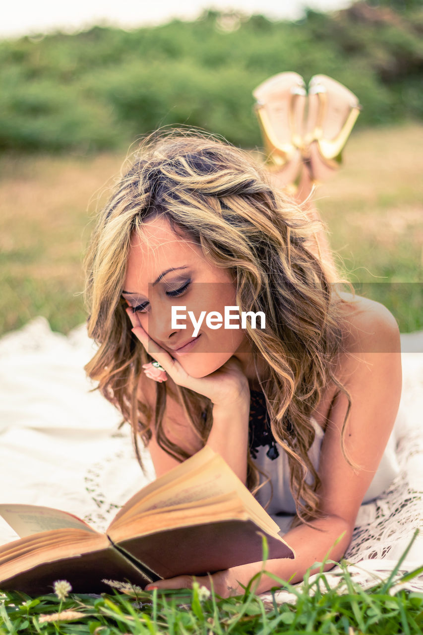 Portrait of romantic young woman reading a book lying down over the grass