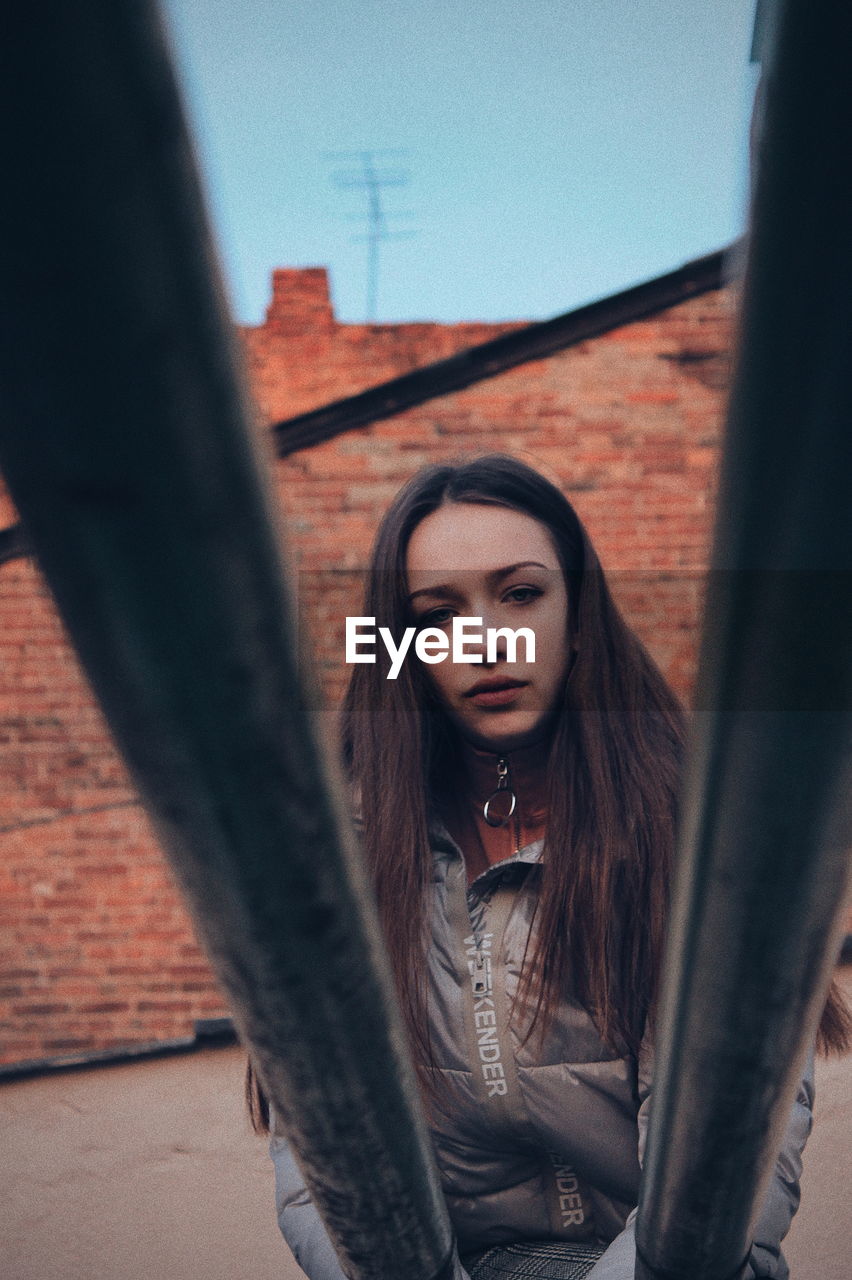 PORTRAIT OF YOUNG WOMAN STANDING AGAINST BUILT STRUCTURE