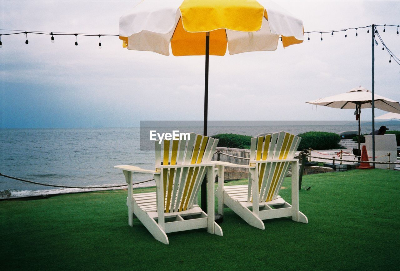 Empty chairs and tables on beach against sky