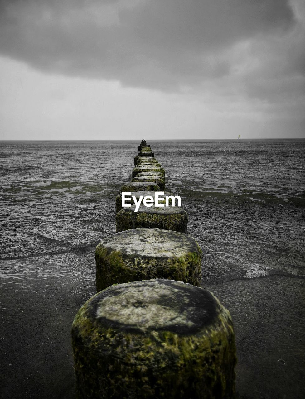 WOODEN POSTS ON SEA AGAINST SKY