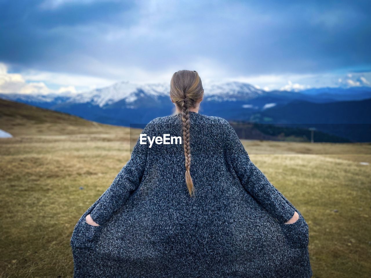 Woman with long hair caught in a ponytail wearing a pullover and looking at the snowcapped mountains