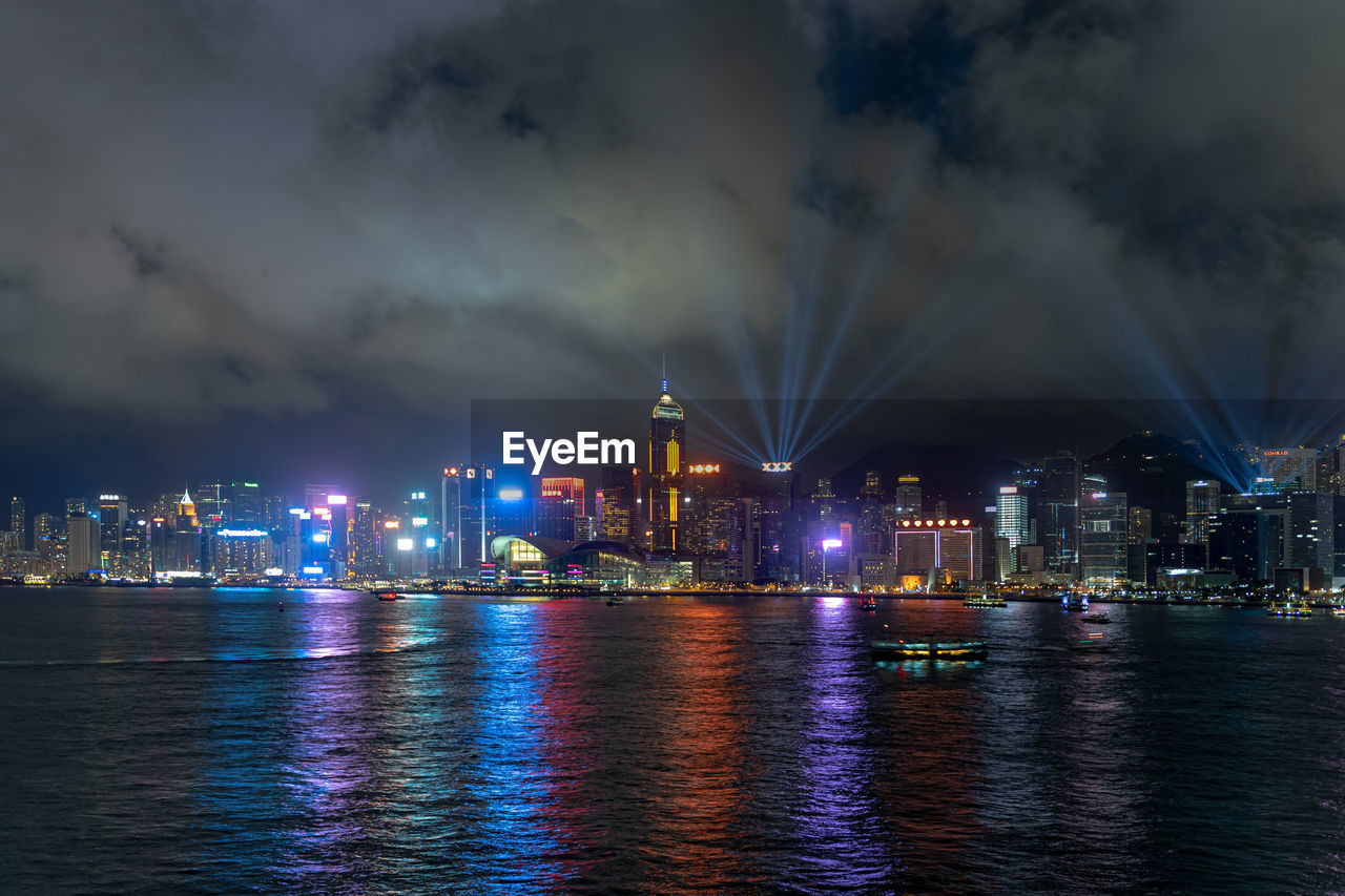 Illuminated buildings by river against sky at night