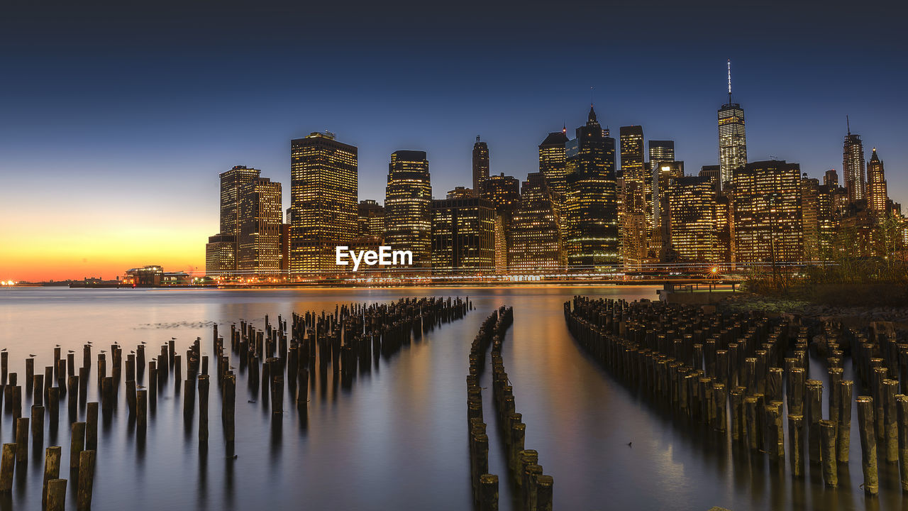 Wooden posts in east river against manhattan skyline during sunset