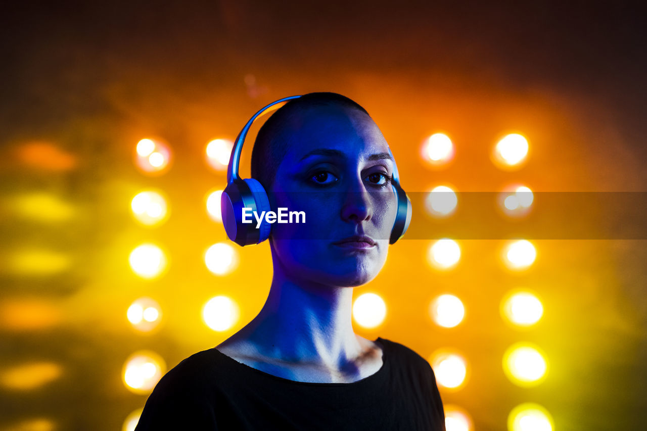 Serious young woman wearing headphones in front of neon lights