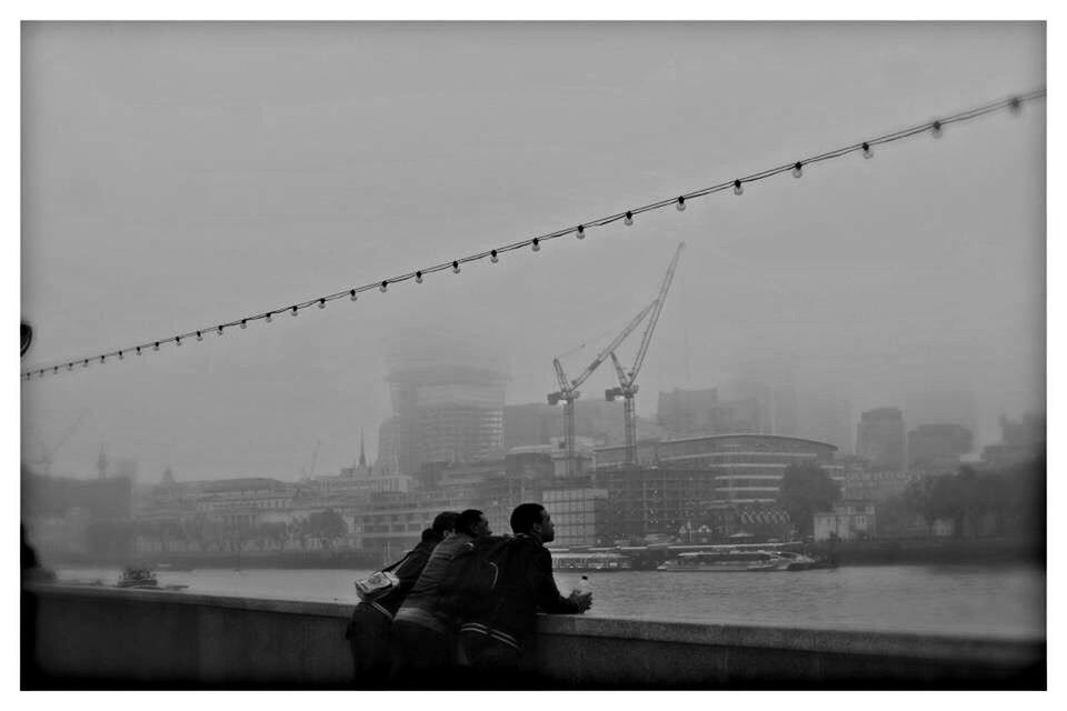 Friends standing by sea and city against sky during foggy weather