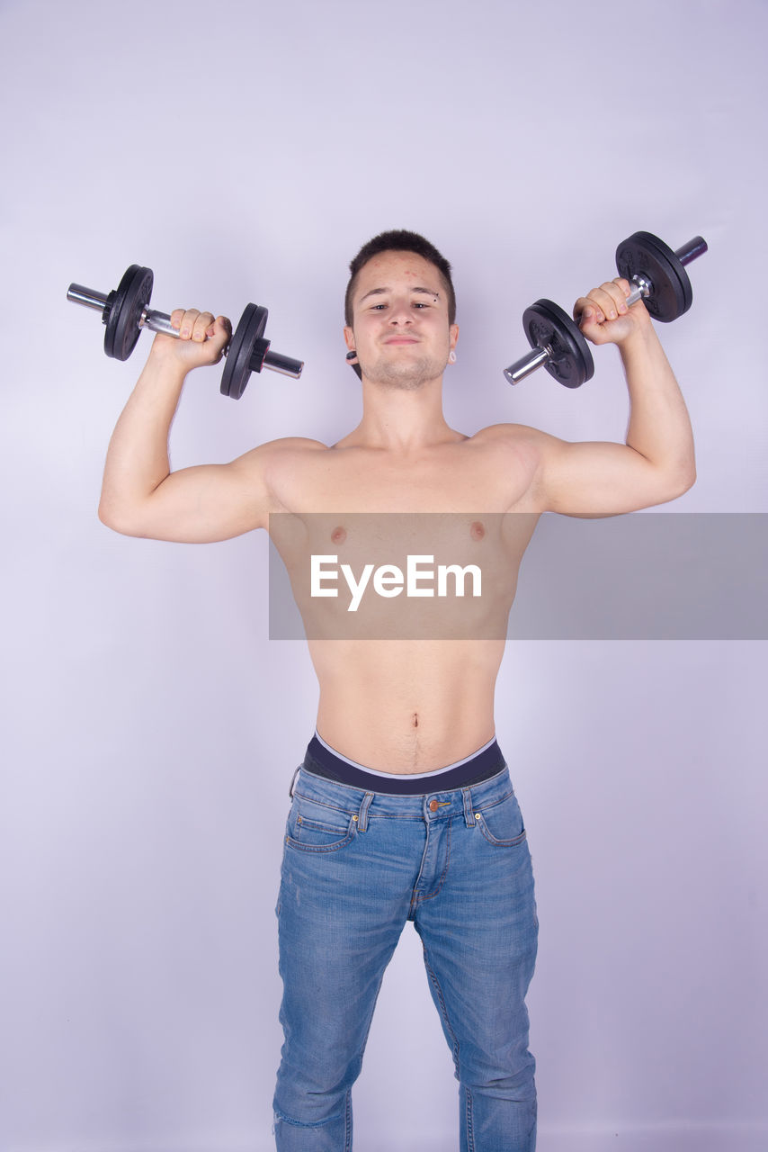 Shirtless man lifting dumbbells against purple background