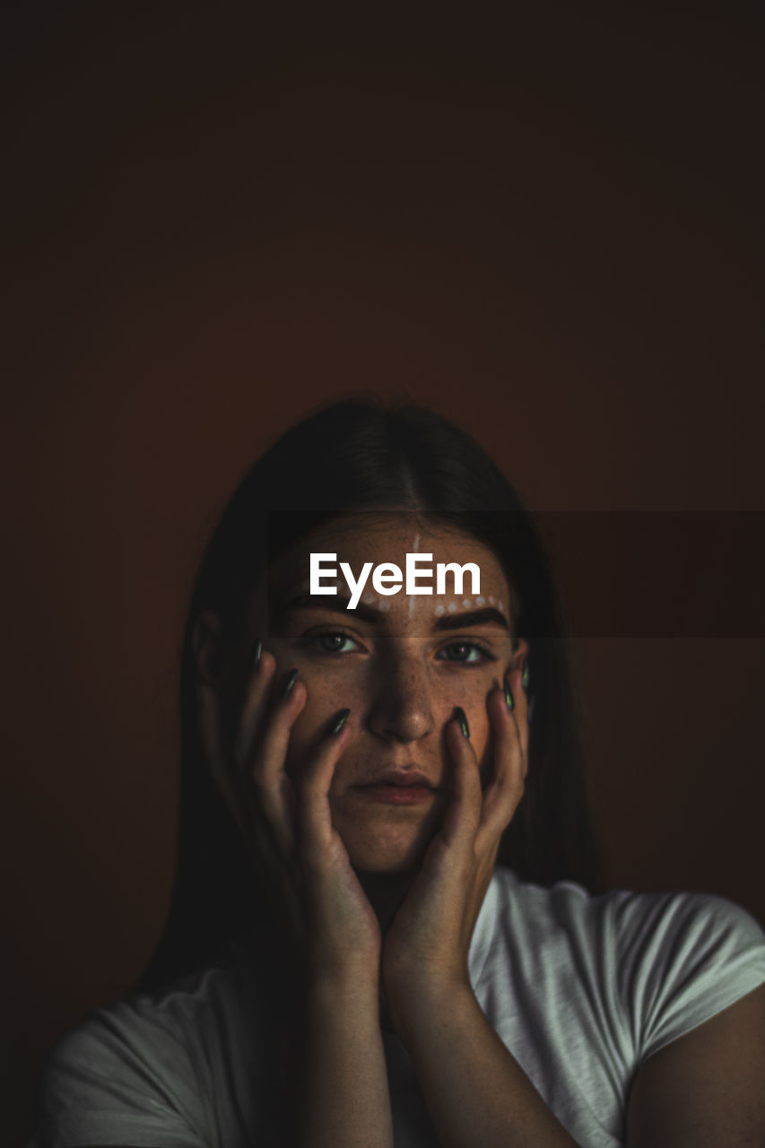 Close-up portrait of young woman with make-up against brown background