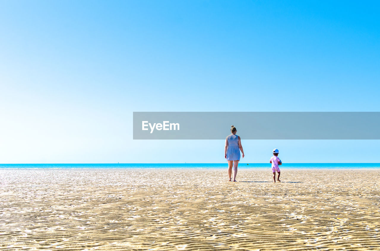 Mother and child walking on a sandbank during low tide at camber sands, east sussex, england