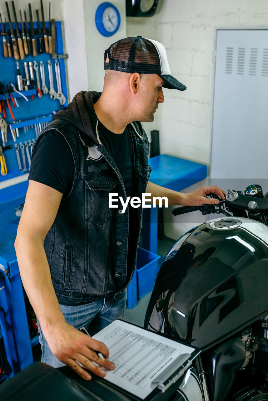 Side view of mature mechanic examining motorcycle in garage