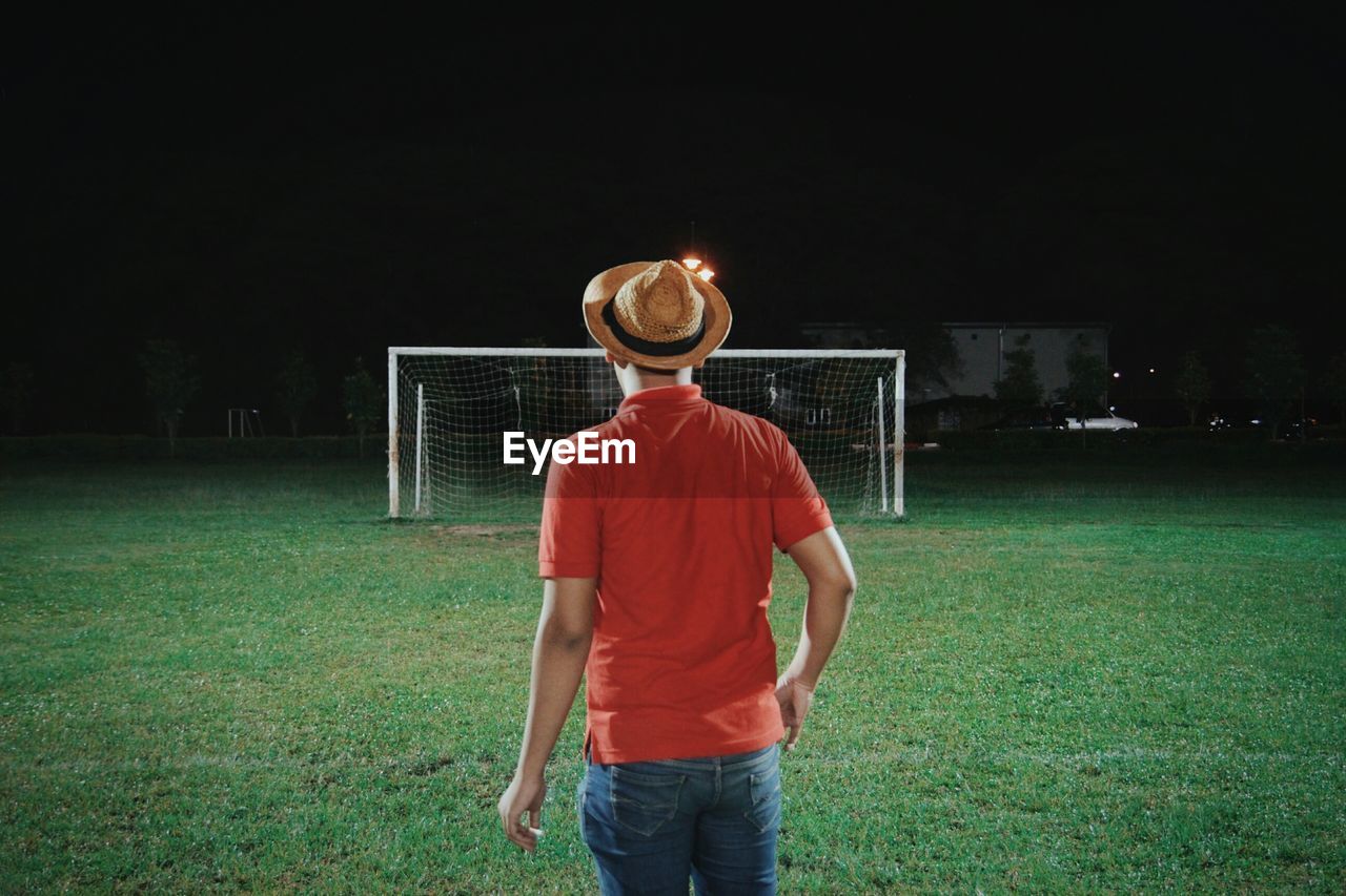 Rear view of man standing against goal post at night