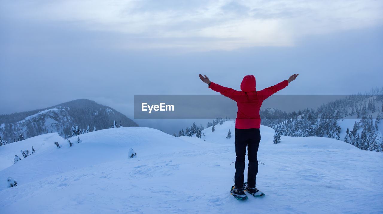 REAR VIEW OF WOMAN STANDING ON SNOWCAPPED MOUNTAIN