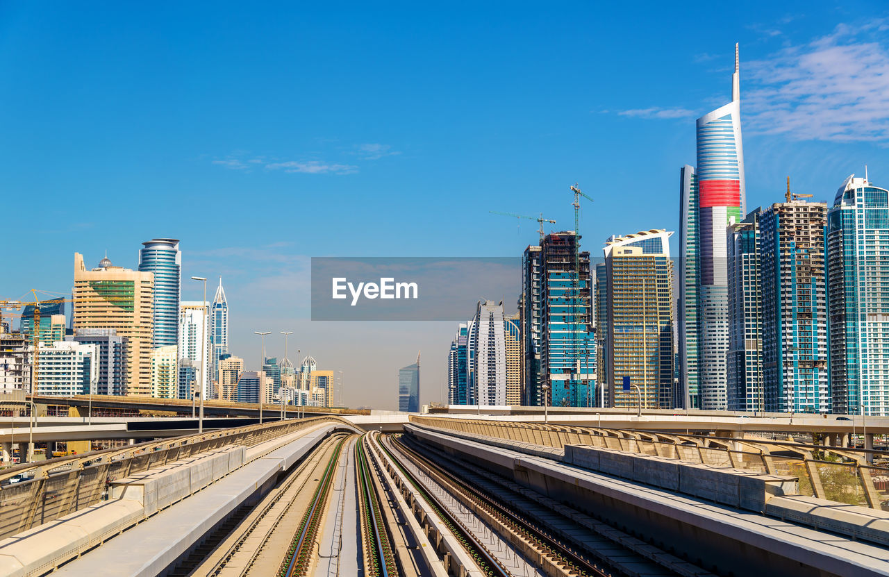 RAILROAD TRACKS BY BUILDINGS AGAINST SKY IN CITY