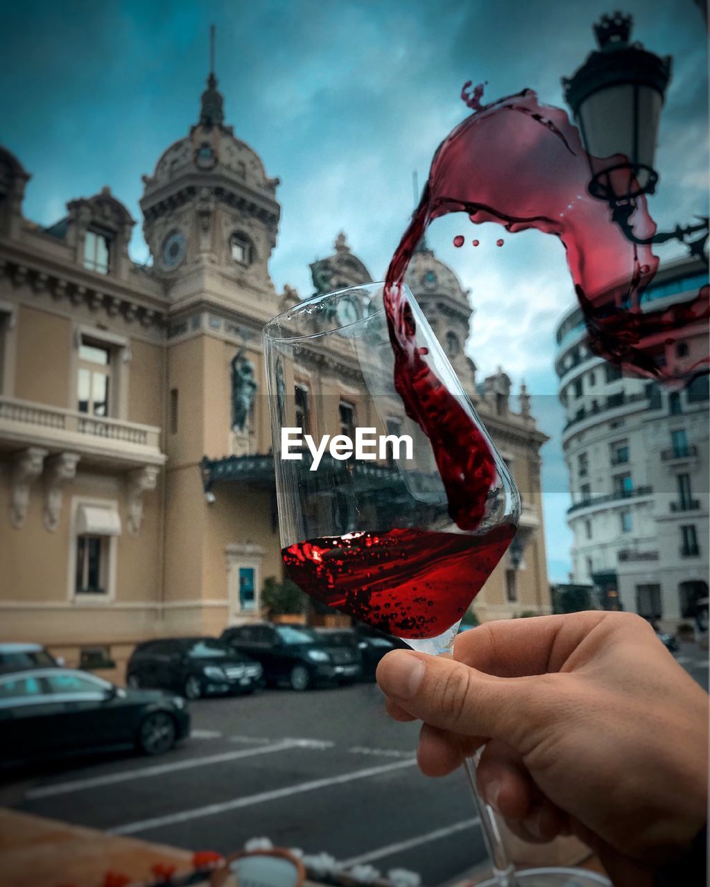 Cropped hand of person holding drink spilling from glass against buildings