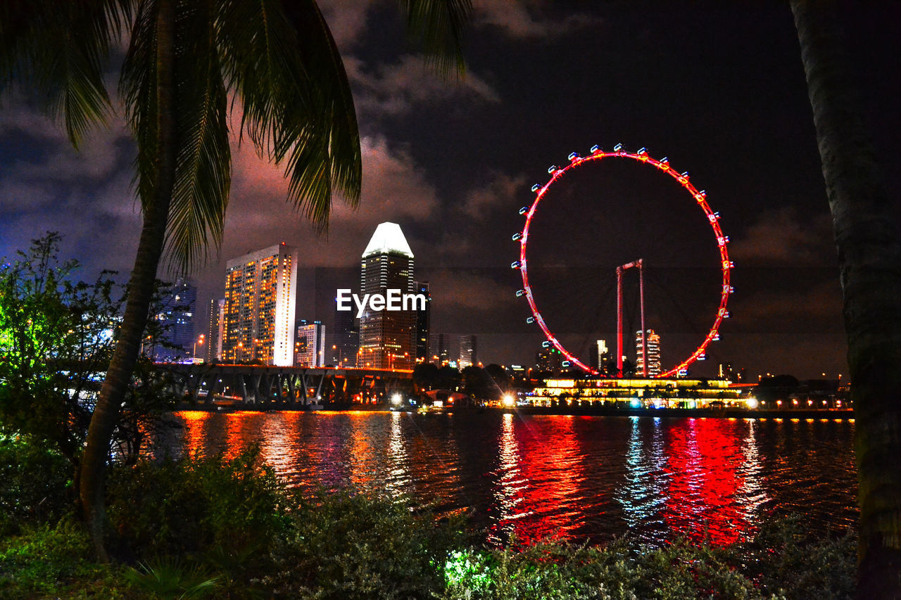 ILLUMINATED FERRIS WHEEL BY RIVER AGAINST SKY IN CITY