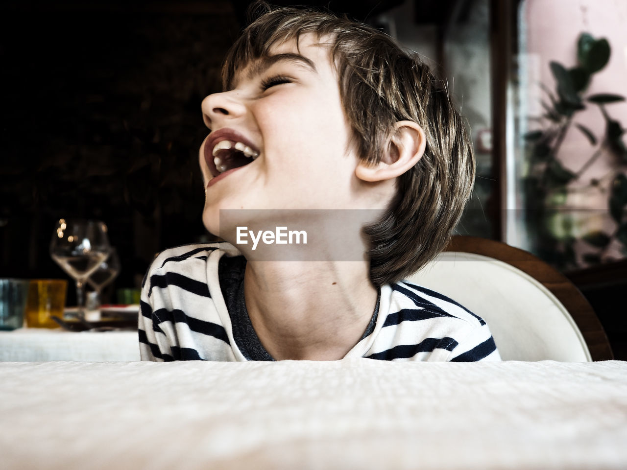 Close-up of boy laughing while sitting on chair by table