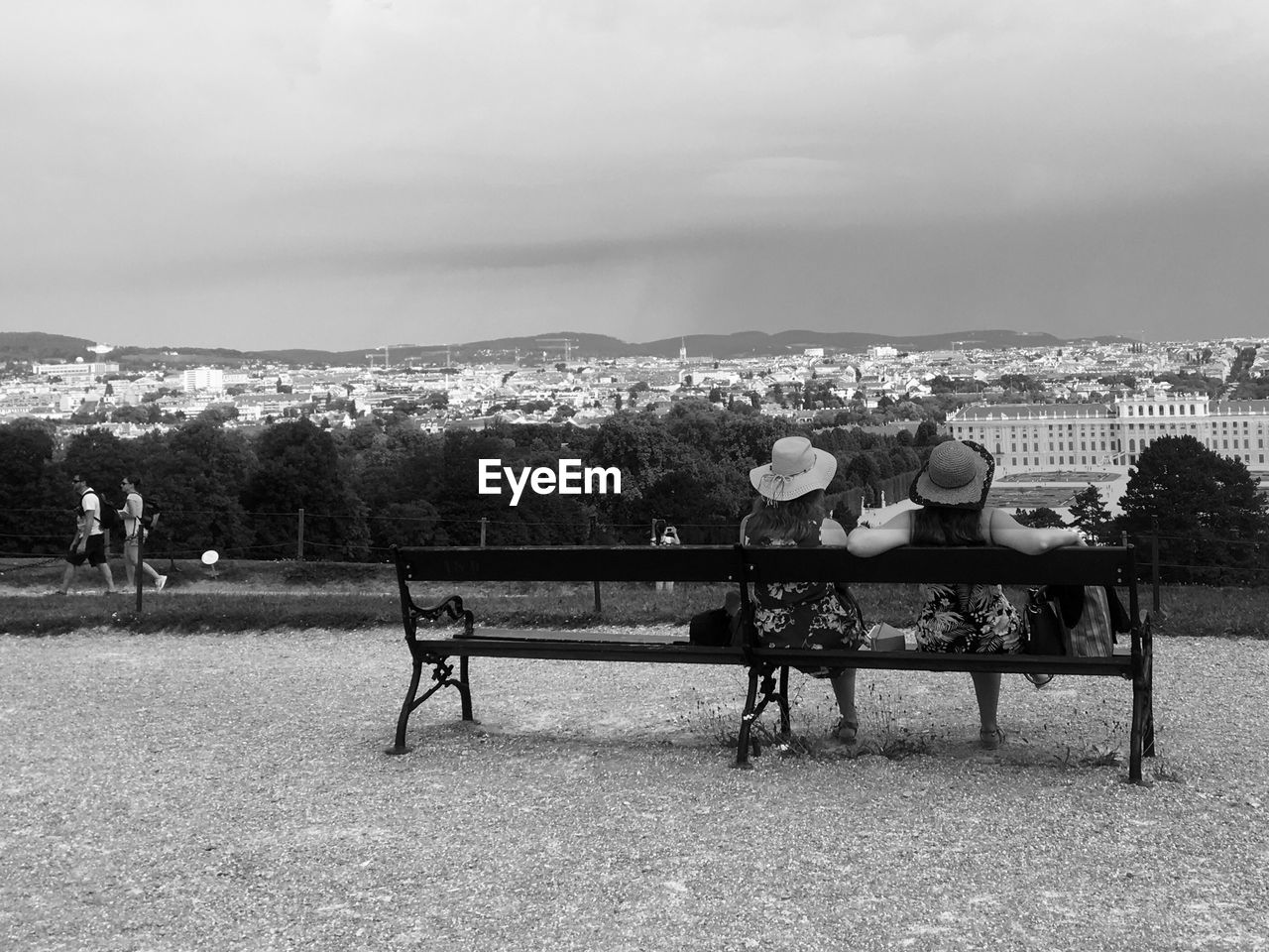 REAR VIEW OF PEOPLE SITTING ON BENCH IN PARK