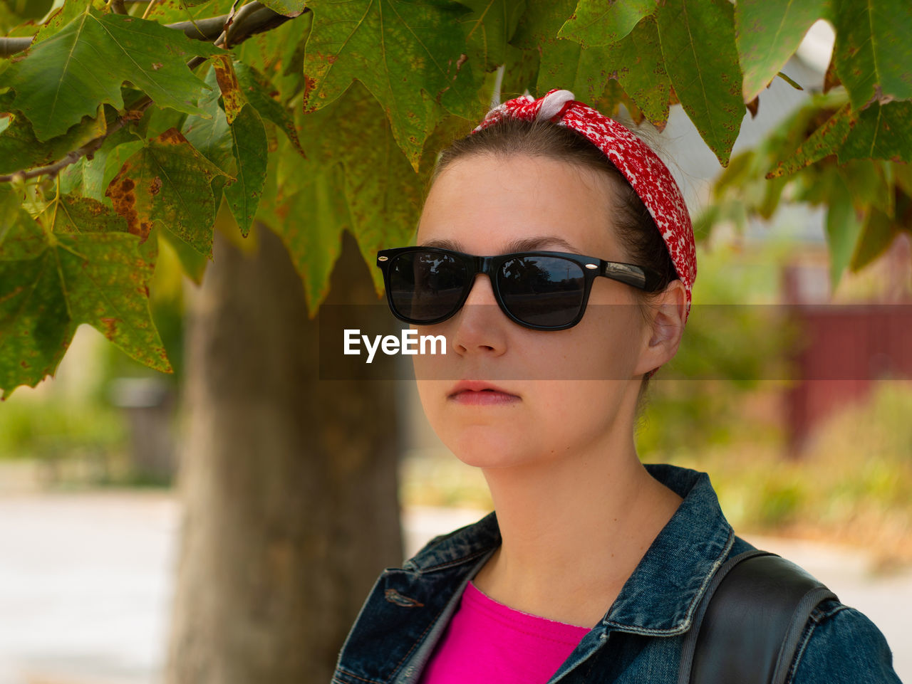 Pretty hipster woman in sunglasses, pink shirt, red bandana and denim jacket on sunny autumn nature.