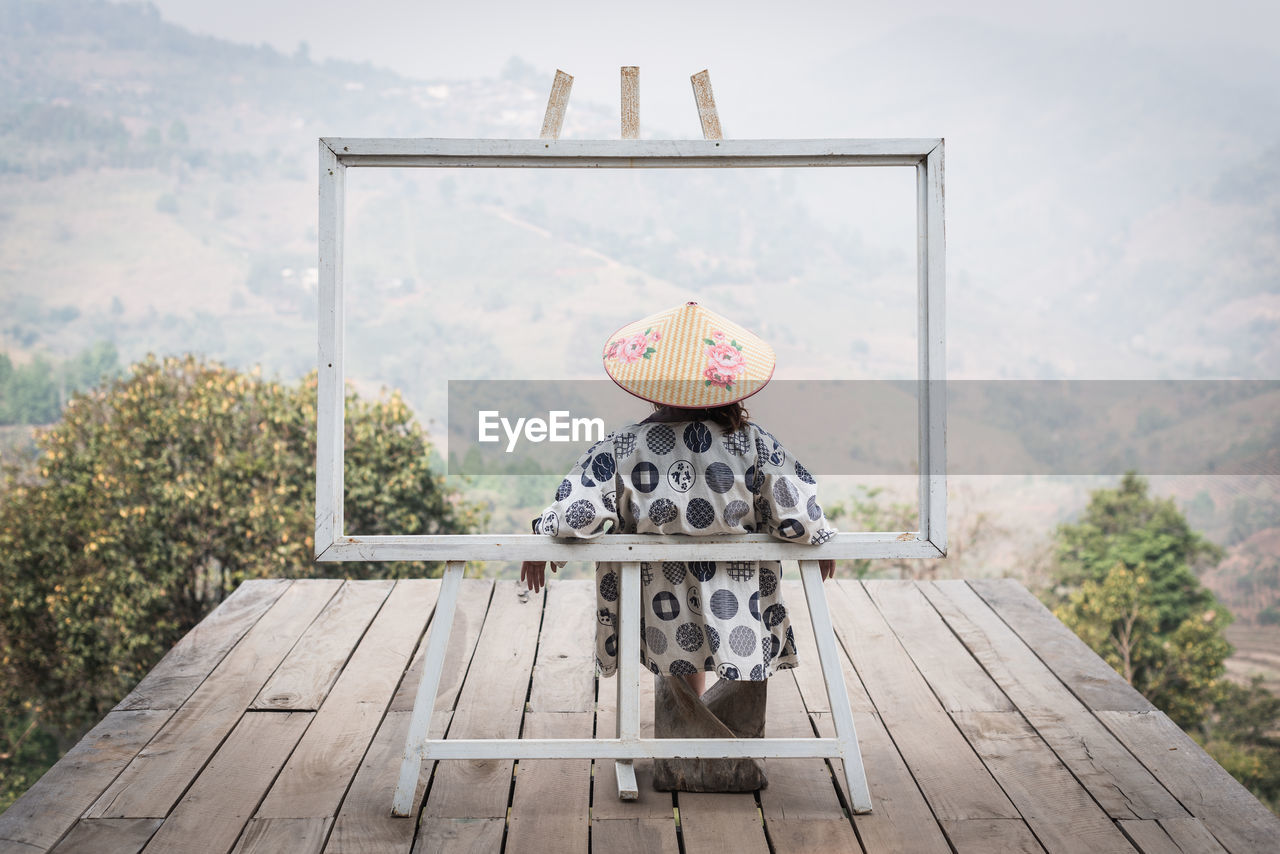 Lady with yukata shirt and bamboo hat in the frame against mountain scenic view