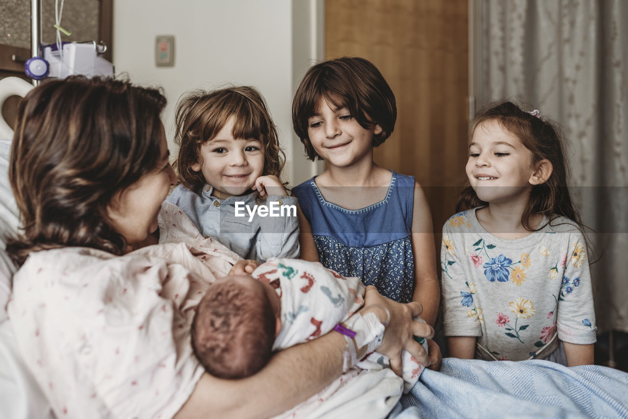 Side view of mother holding newborn son meeting siblings