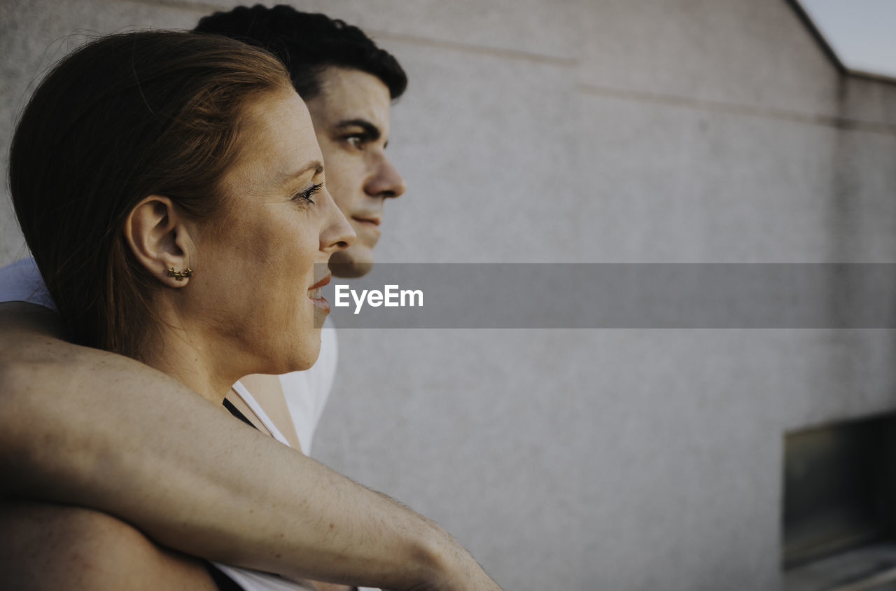 Side view of woman and man looking away against wall