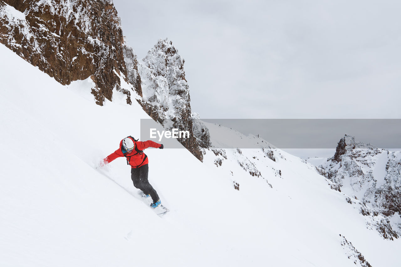 Snowboarder riding down mountain in red jacket