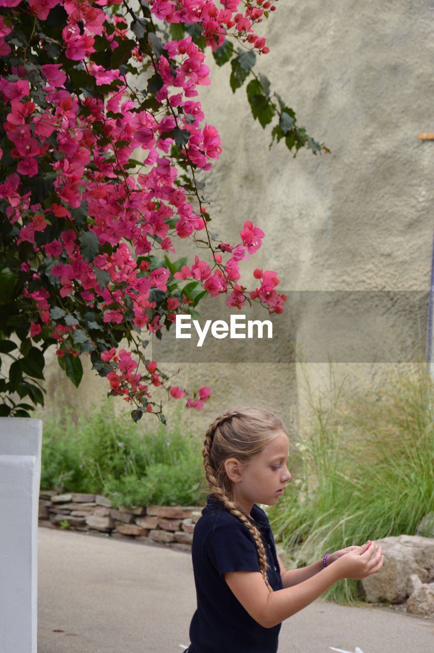 Side view of girl with pink flower against plants