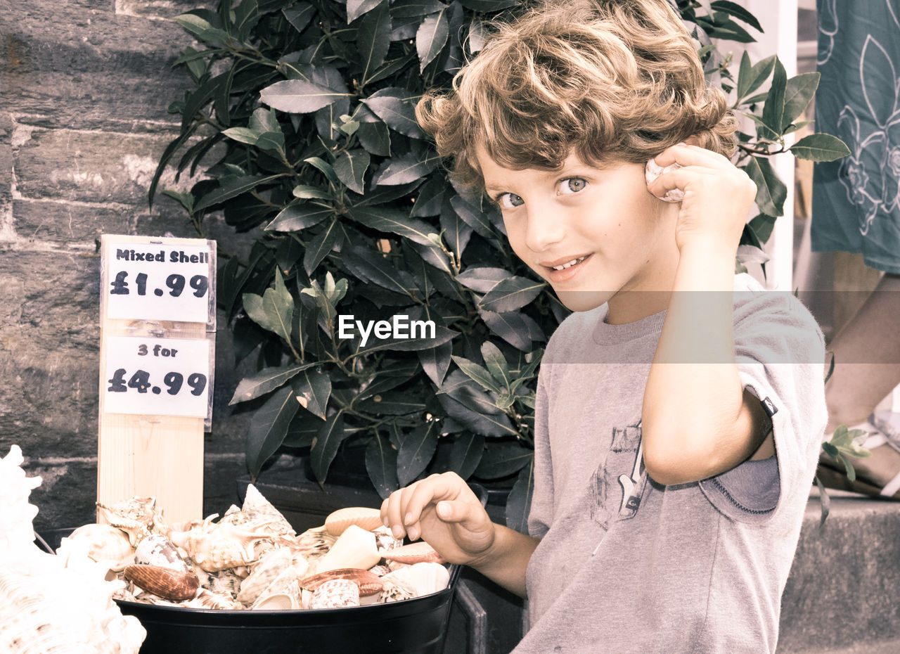 Portrait of smiling boy listening to seashell at market stall