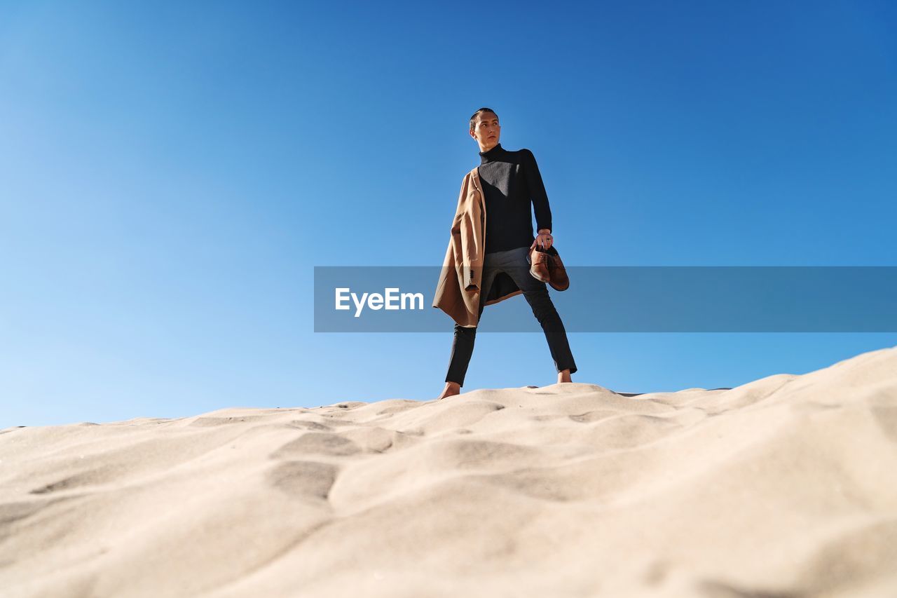 Low angle view of man standing on desert against clear blue sky