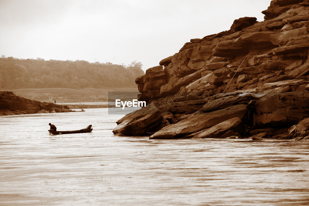 Man on boat in sea by mountain against sky