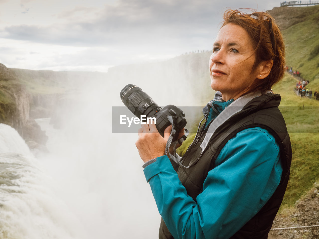 Side view of woman photographing against waterfall