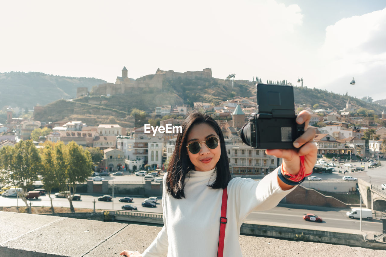 Smiling woman taking selfie while standing against buildings