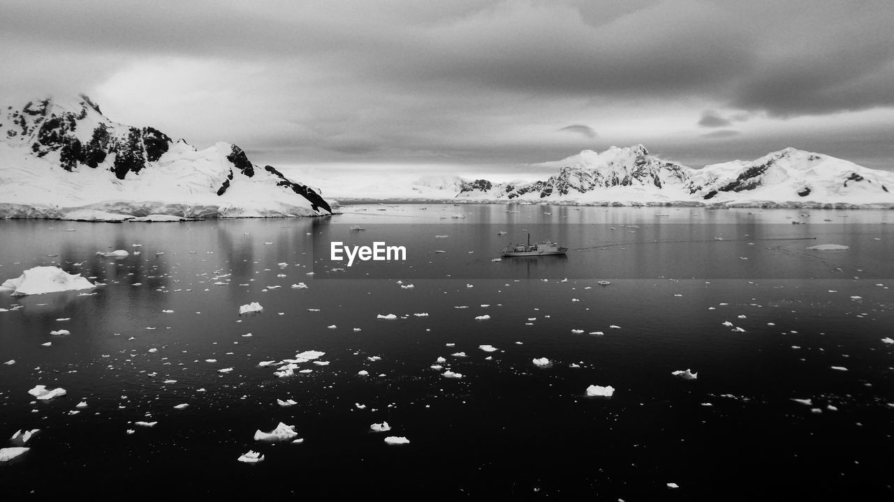 Black and white photo of sea with icebergs and ship against snowcapped mountains in antarctica