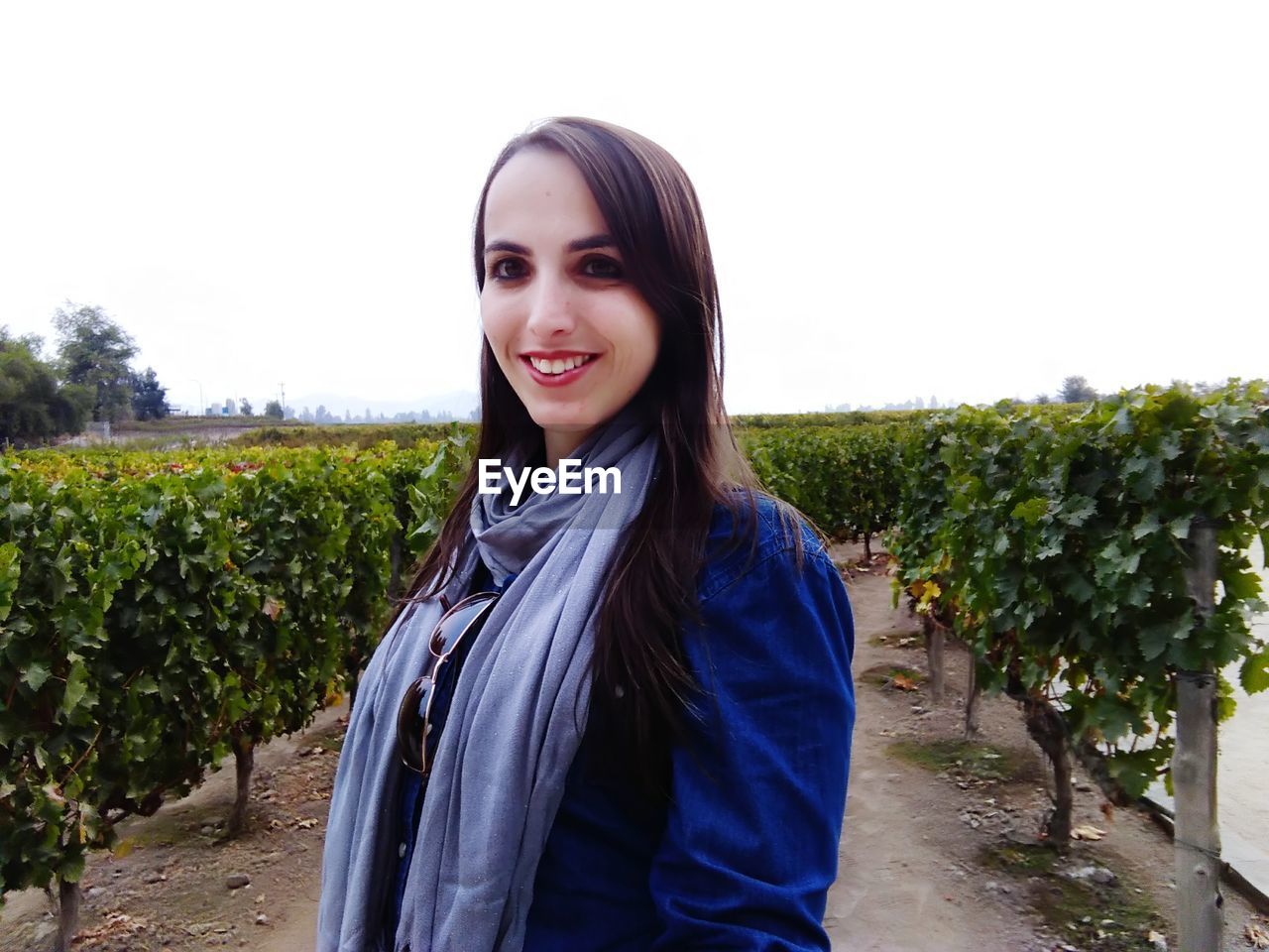 Portrait of smiling young woman standing in vineyard against sky