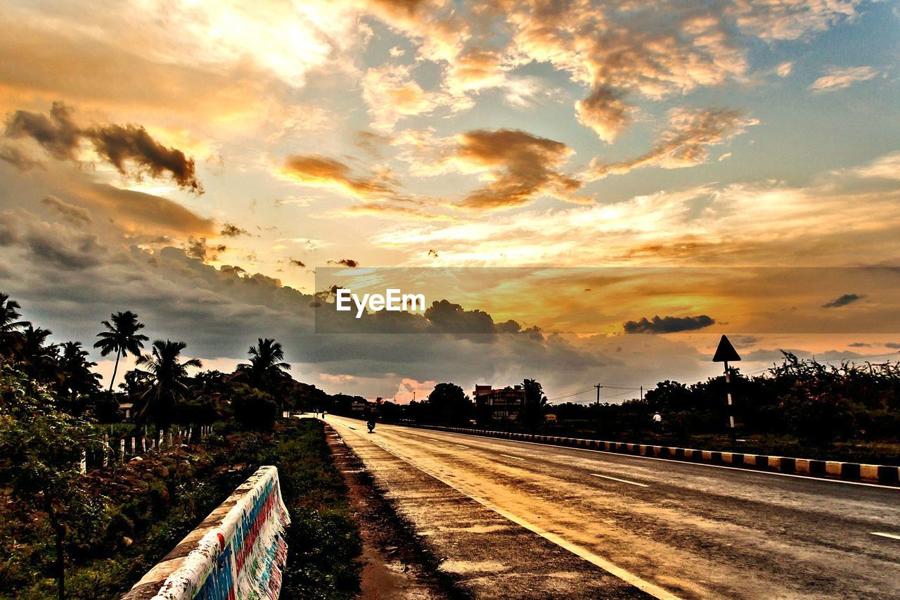 Road amidst trees against sky during sunset