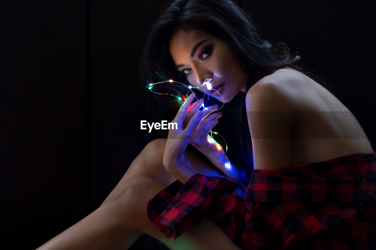 Portrait of sensuous young woman holding illuminated string lights