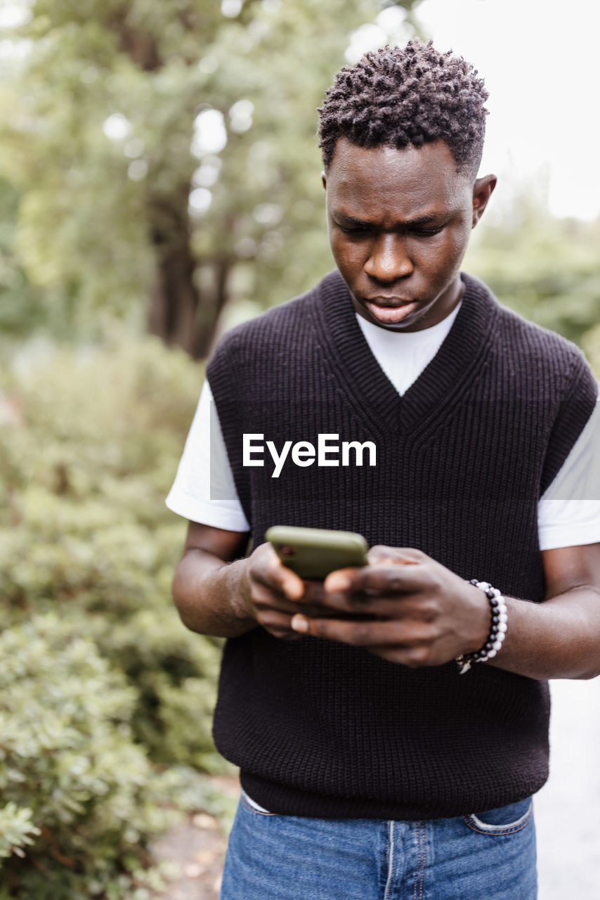 Young sad african man typing message, texting on phone outdoor