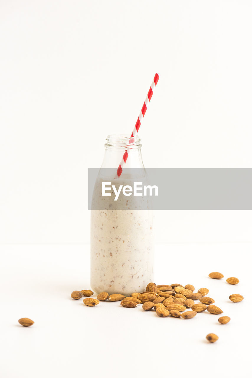 Milk bottle with almonds against white background