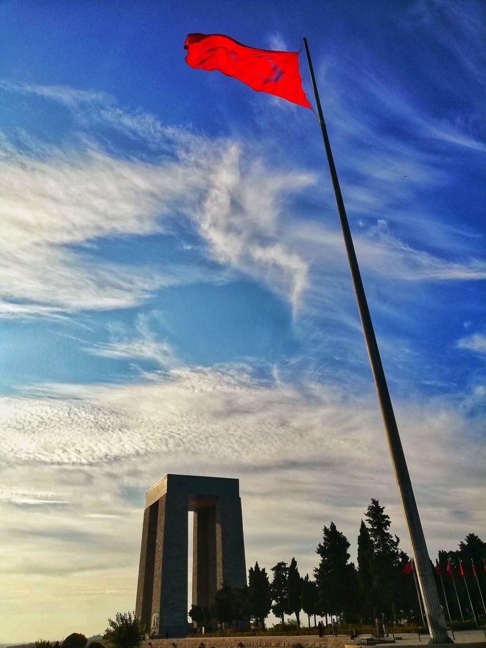 flag, sky, patriotism, cloud, architecture, nature, built structure, low angle view, building exterior, no people, environment, red, outdoors, day, wind, city, blue, tree, plant, travel destinations