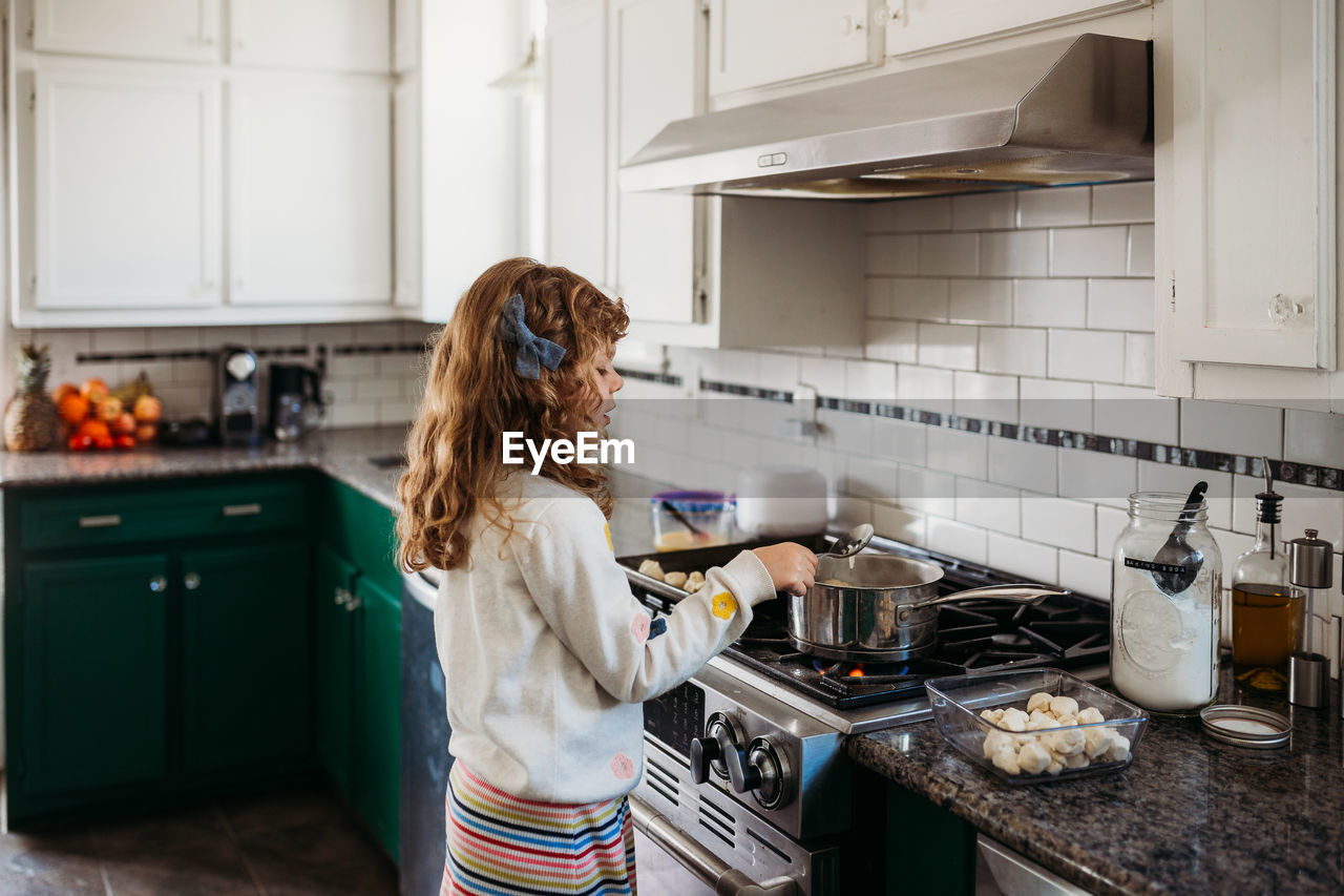 Young girl cooking pretzel dough on stovetop in modern kitchen